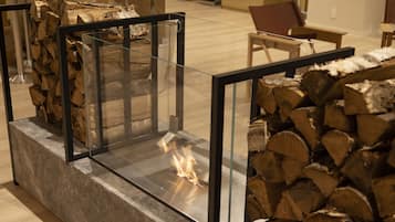 A glass-enclosed fireplace with a visible fire, surrounded by stacked firewood.