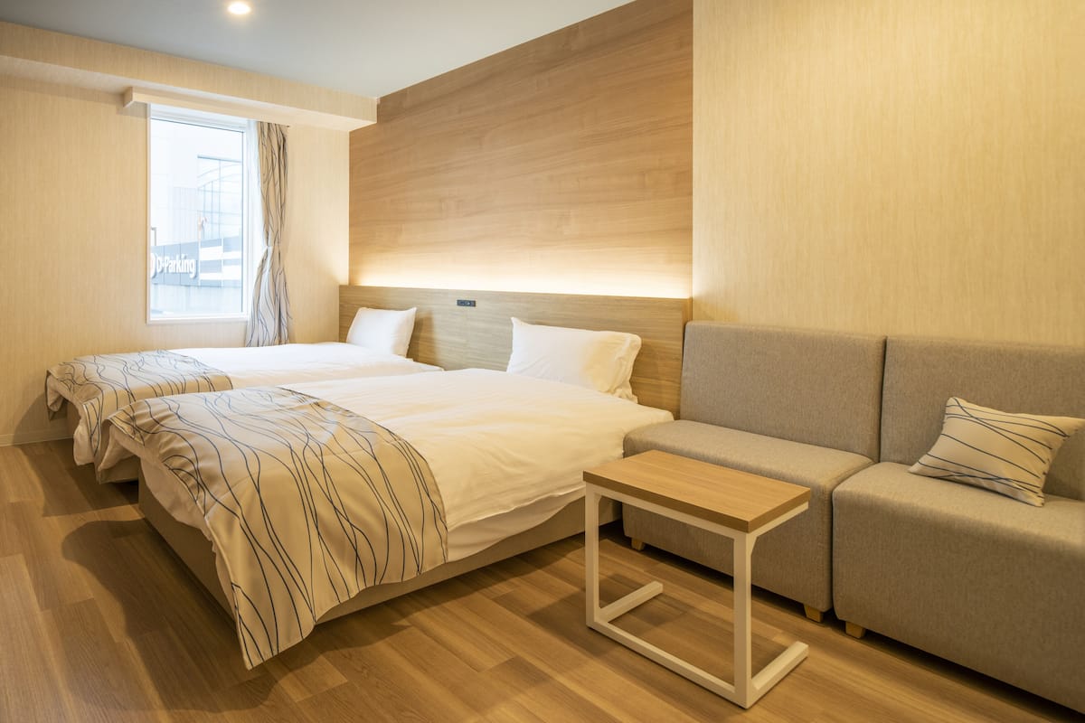 Une chambre d’hôtel avec deux lits, un canapé, une petite table et une fenêtre avec des rideaux.