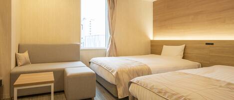 A hotel room with a sofa, two single beds, a small table, and a window with curtains.