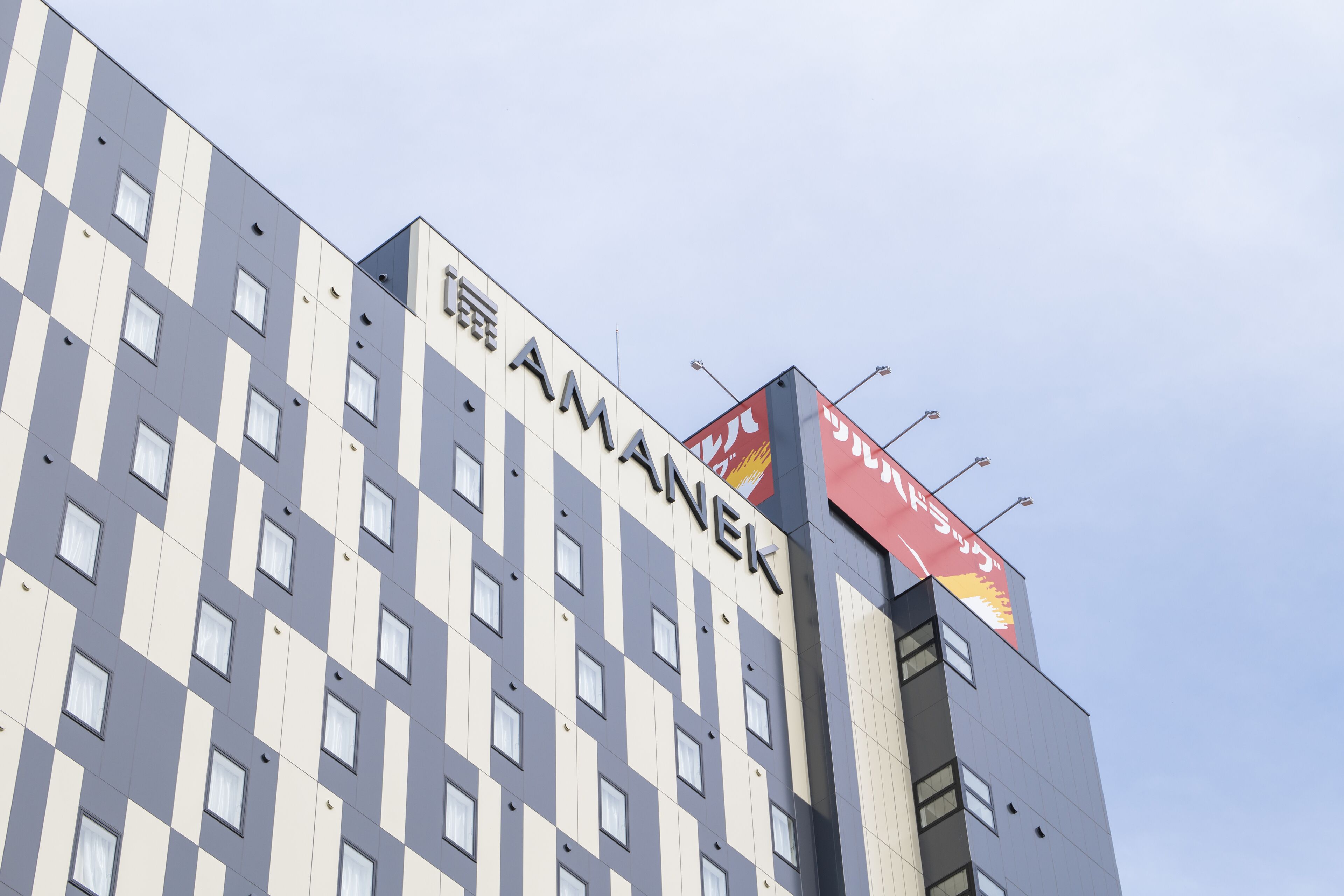 Un edificio con fachada a cuadros y el nombre "AMANEK" exhibido destacadamente.
