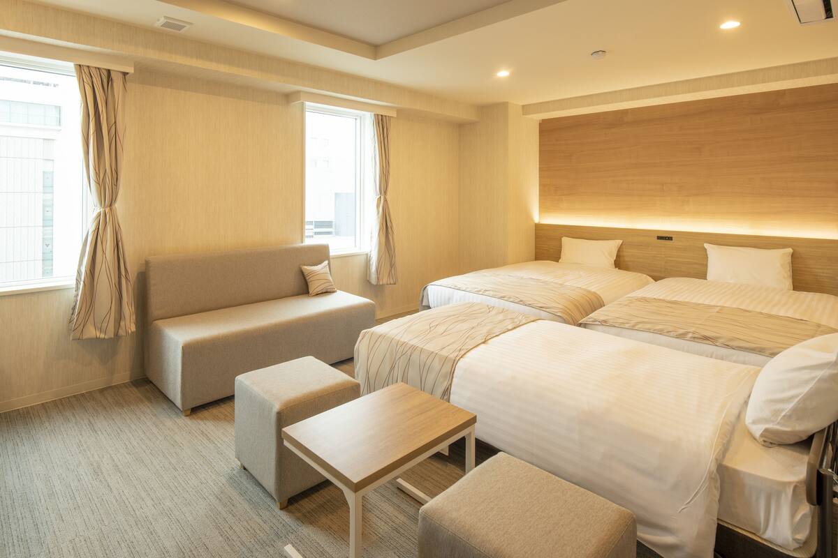 Une chambre d’hôtel avec un canapé, deux lits, une petite table et une fenêtre avec des rideaux.