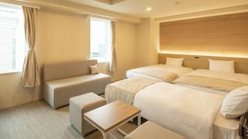 A hotel room with a sofa, two beds, a small table, and a window with curtains.