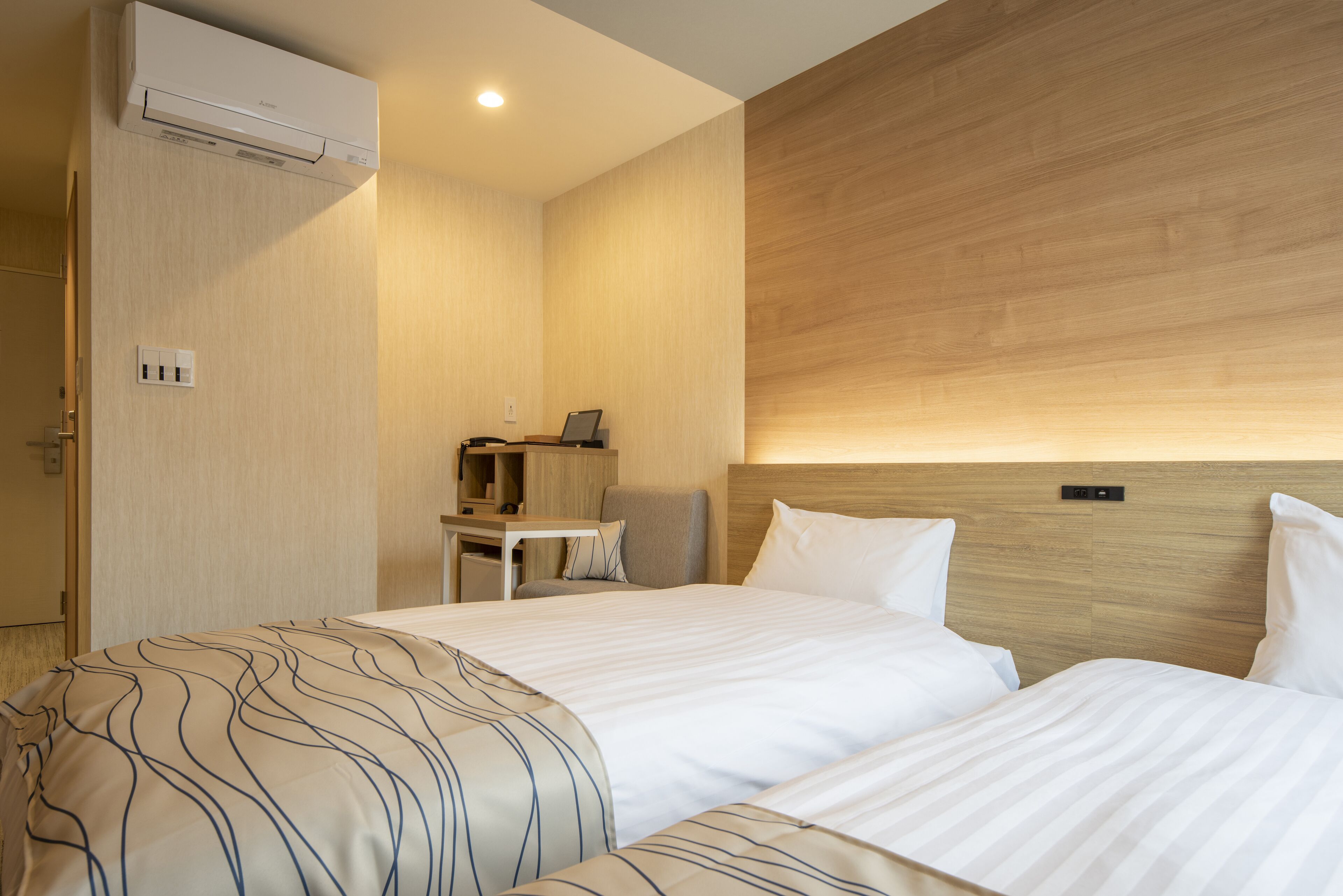 A hotel room with two beds, a desk, and a chair.