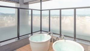 Een moderne badkamer met twee ruime badkuipen en stadszicht door grote ramen.