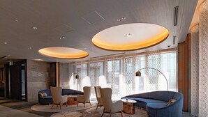 A modern hotel lobby with a seating area featuring sofas and chairs, large windows with patterned curtains, and a circular ceiling light fixture. - Daiwa Roynet Hotel Osaka Sakaisuji Honmachi PREMIER (Osaka)