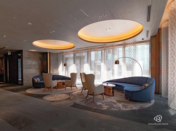 A modern hotel lobby with a seating area featuring sofas and chairs, large windows with patterned curtains, and a circular ceiling light fixture. - Daiwa Roynet Hotel Osaka Sakaisuji Honmachi PREMIER (Osaka)
