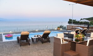 An outdoor pool area with lounge chairs, a table with a laptop, and a view of the sea. - Aurora Luxury Retreat - Beachfront & Private Pool (Messini)