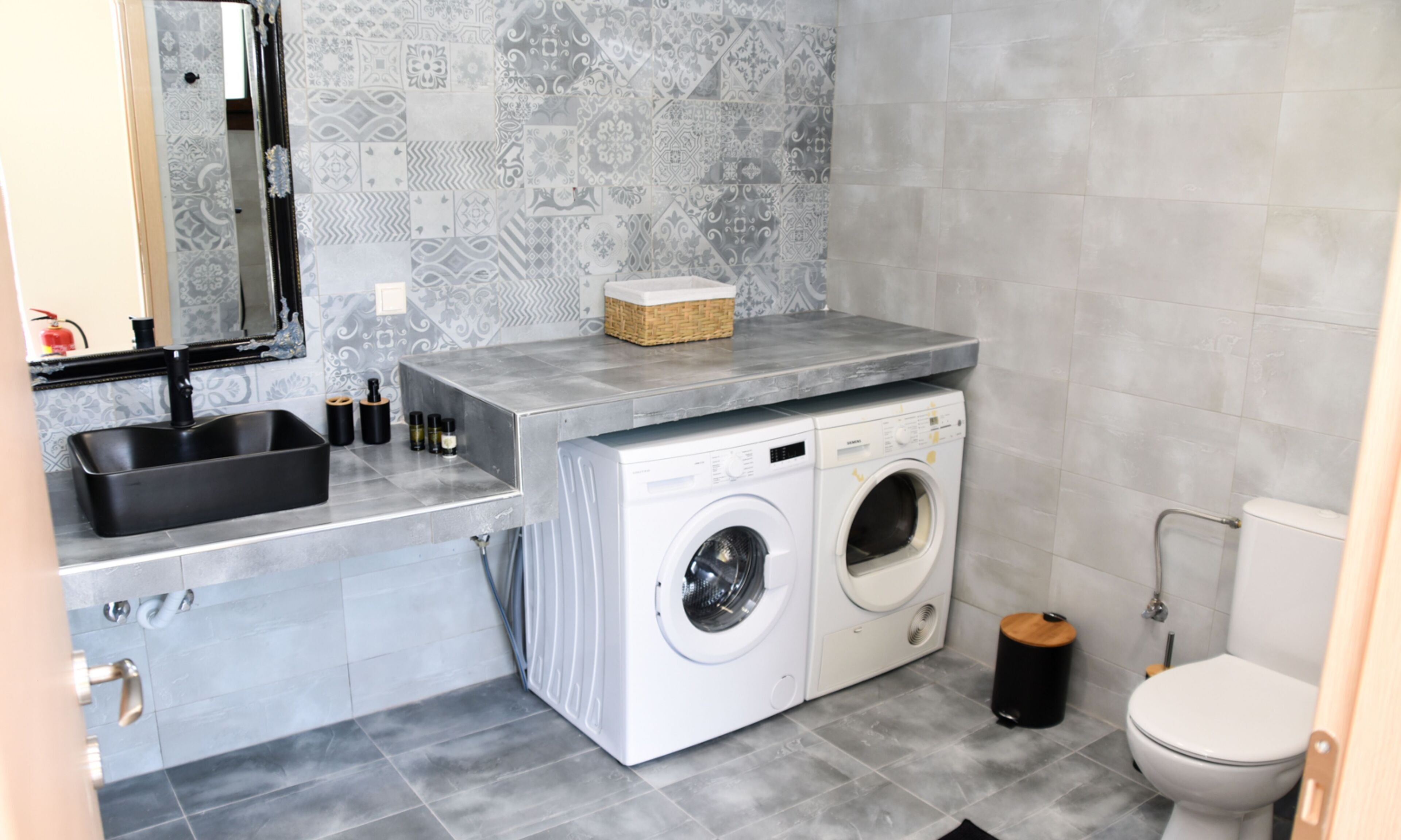 Une salle de bain moderne avec des carreaux gris, un lavabo encastré, un lave-linge et des toilettes.