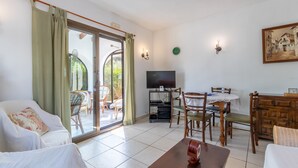 Een woonkamer met een bank, eettafel, stoelen, een televisie en een schuifpui naar buiten.