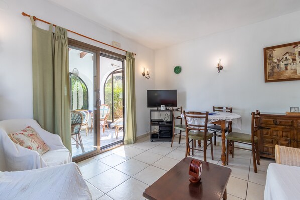 A living room with a sofa, dining table, chairs, a TV, and a sliding glass door to the outside.