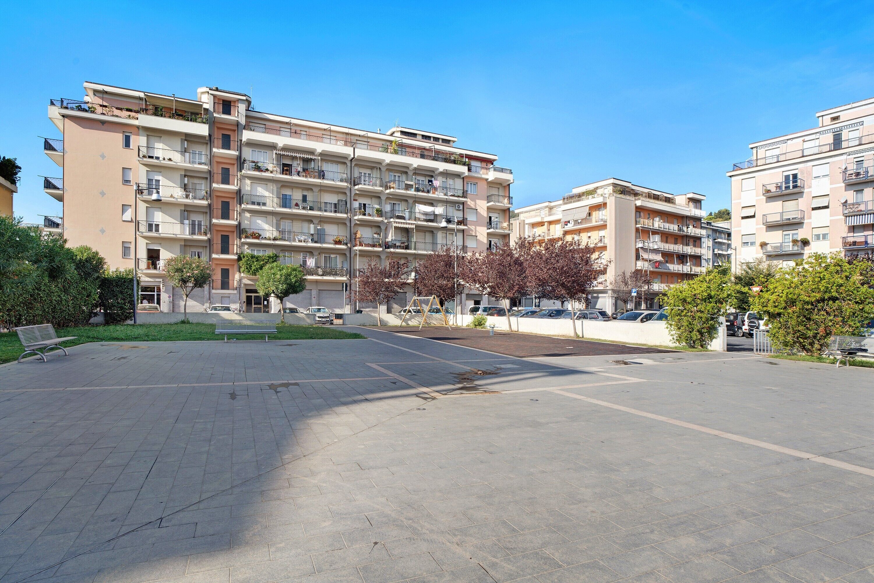 Un immeuble résidentiel à plusieurs étages, doté de balcons, d’une cour pavée et surplombant un ciel dégagé.