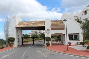 Une entrée fermée par un portail mène à un bâtiment doté d’un toit en tuiles, une enseigne indique « LOMBAS », et une route pavée y conduit.
