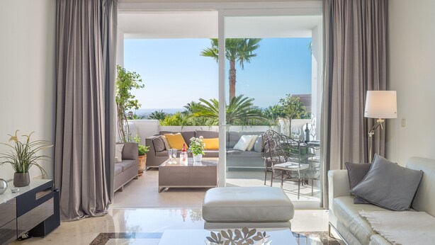 A modern living room with a sofa, a coffee table, and a balcony with a view of palm trees. - Apartment "Seaview Flat Benahavis-Marbella" with Sea View, Pool, Wi-Fi, Terrace & Garden (Benahavis)
