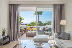 A modern living room with a sofa, a coffee table, and a balcony with a view of palm trees. - Apartment "Seaview Flat Benahavis-Marbella" with Sea View, Pool, Wi-Fi, Terrace & Garden (Benahavis)