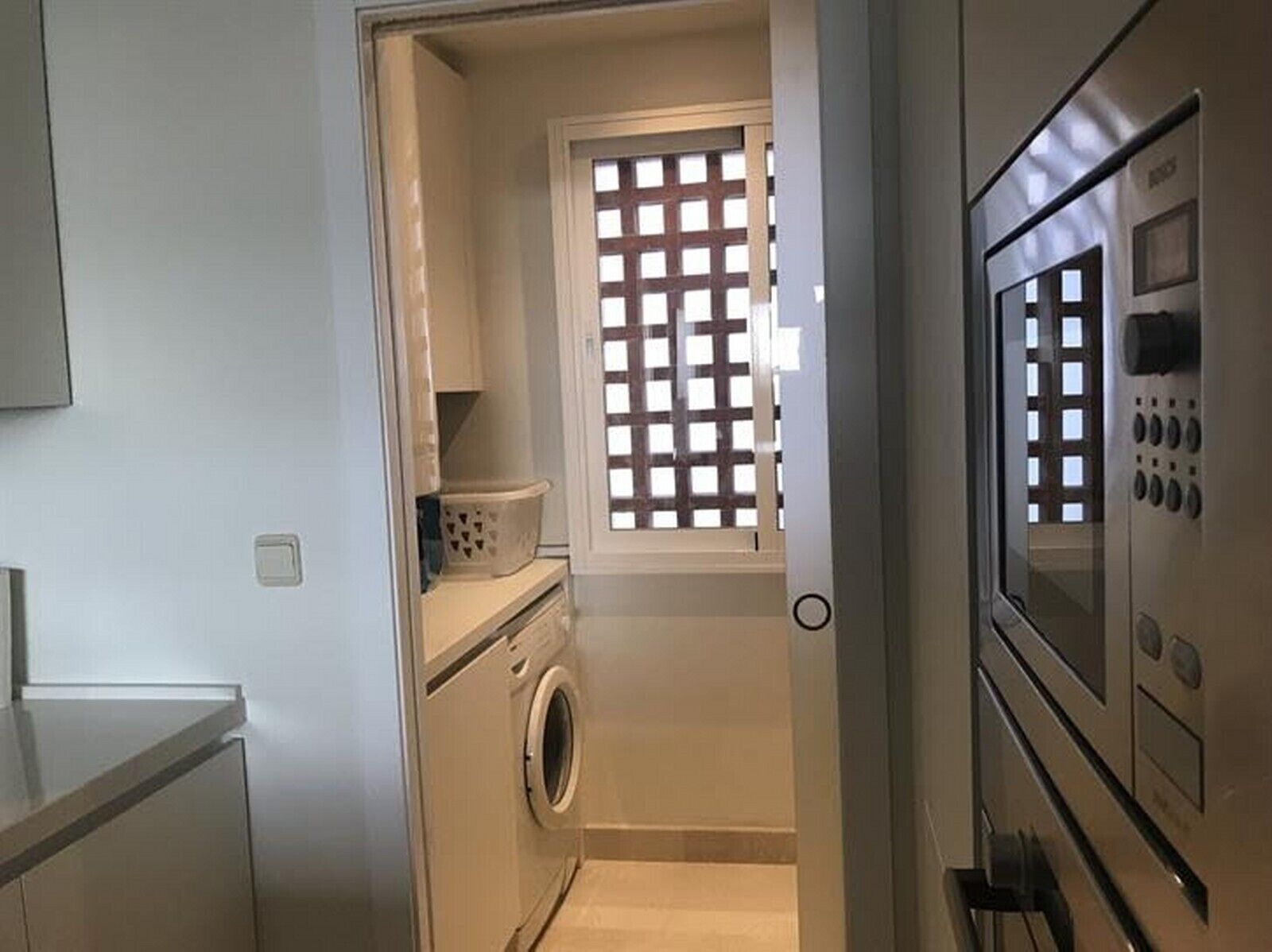 A laundry room with a washing machine, a dryer, and a window with a grid pattern.