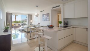 A modern kitchen with white cabinetry, a central island, and a dining area with a view. - Apartment "Seaview Flat Benahavis-Marbella" with Sea View, Pool, Wi-Fi, Terrace & Garden (Benahavis)