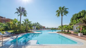 A swimming pool with lounge chairs, palm trees, and a clear sky. - Apartment "Seaview Flat Benahavis-Marbella" with Sea View, Pool, Wi-Fi, Terrace & Garden (Benahavis)