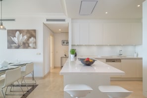 A modern kitchen with white cabinetry, a central island, and a dining area with a glass table and chairs.