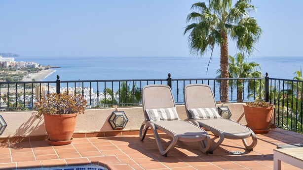 Une terrasse avec deux fauteuils, un pot de fleurs et une vue sur la mer.