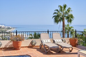 Una terraza con dos sillones de descanso, una planta en maceta y vista al mar.