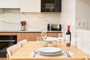 A modern kitchen with a dining table set for two, a Bosch microwave, and a wine bottle.