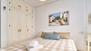 Une chambre à coucher avec une couvre-lit à carreaux, un tableau représentant une scène de rue, une armoire et une table de chevet.
