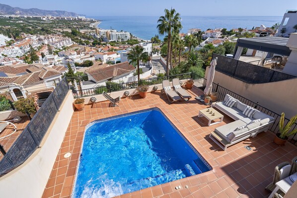 Una piscina en la azotea con vista al mar, sillones de descanso y plantas en macetas.