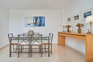 Un coin repas avec une table à plateau de verre, des chaises en métal, un vase, des tableaux encadrés au mur et un buffet en bois agrémenté d’objets décoratifs.
