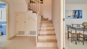 Un escalier menant à une salle à manger avec une table et des chaises, un tableau accroché au mur et une porte dotée d’une grille d’aération.