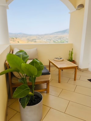 A balcony with a view of a desert landscape, a potted plant, a wooden chair with a cushion, and a small table. - 'Luxurious villa in the sun' with Sea & Mountain View, Pool, A/C & Wi-Fi (Mijas Costa)