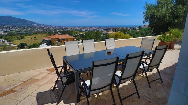 An outdoor patio with a table and chairs, overlooking a scenic view of a town and mountains. - 'Luxurious villa in the sun' with Sea & Mountain View, Pool, A/C & Wi-Fi (Mijas Costa)