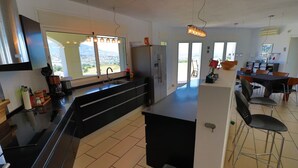 A modern kitchen with a large island, a dining area with chairs, and a view of the city. - 'Luxurious villa in the sun' with Sea & Mountain View, Pool, A/C & Wi-Fi (Mijas Costa)