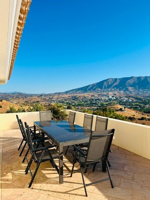 Um pátio externo com mesa e cadeiras, com vista para uma paisagem montanhosa.