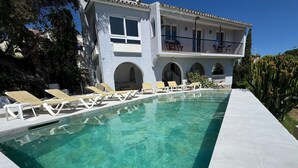 A swimming pool with lounge chairs, a building with balconies, and a clear sky. - 'Nice and Spacius Villa near Fuengi' with Sea & Mountain View, Pool, NO under 40 (Mijas)