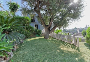 Un jardín bien cuidado con un gran árbol, una cerca blanca y un edificio al fondo.