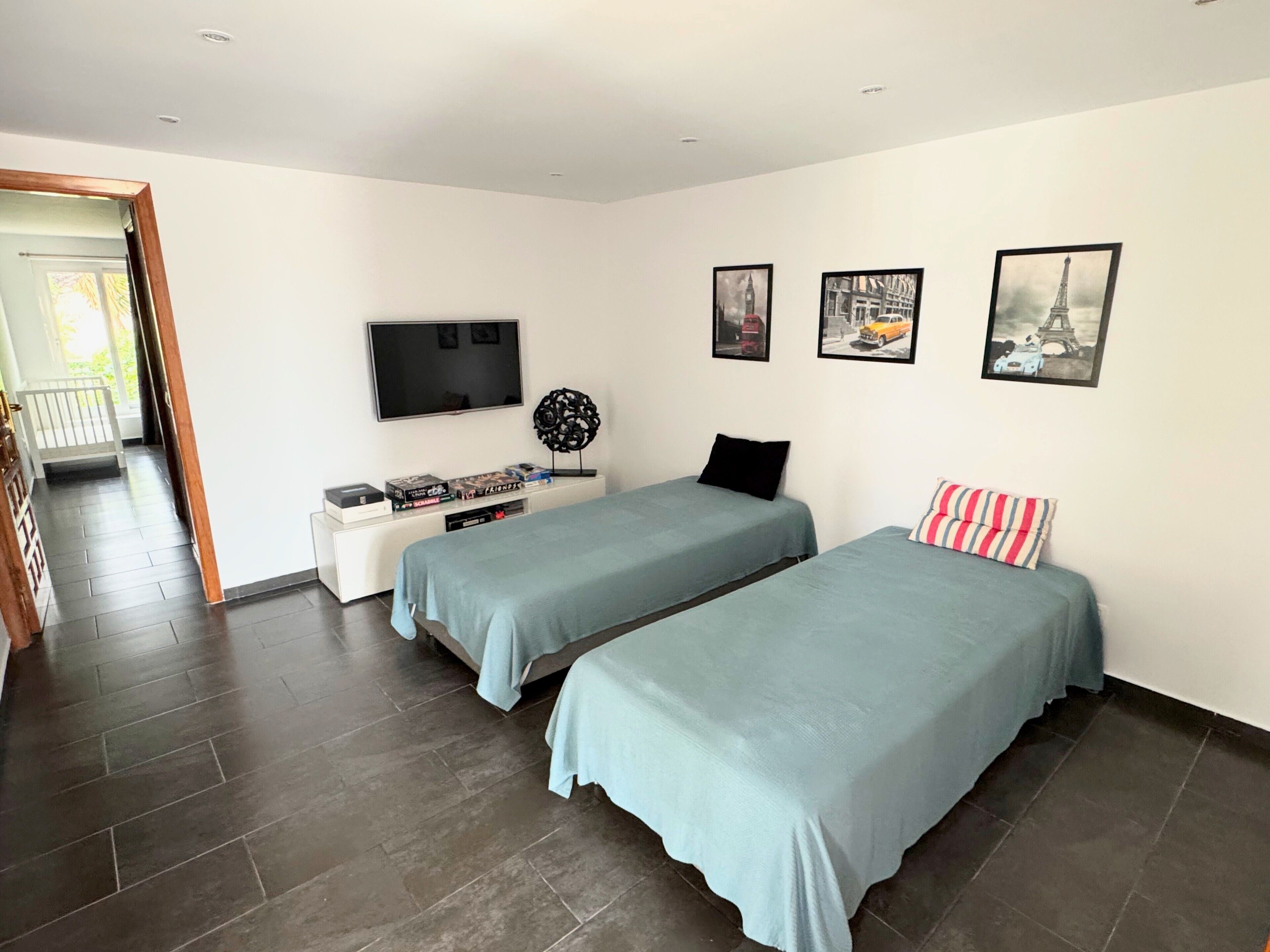 A bedroom with two beds, a TV, a small table with books, and a door leading to a balcony.