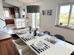 Un comedor con mesa preparada para cuatro, una cocina al fondo y un balcón con vistas.