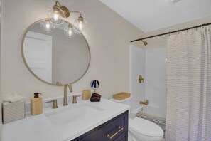 Une salle de bain avec un miroir rond, un lavabo blanc, un meuble sombre, des toilettes et un rideau de douche.