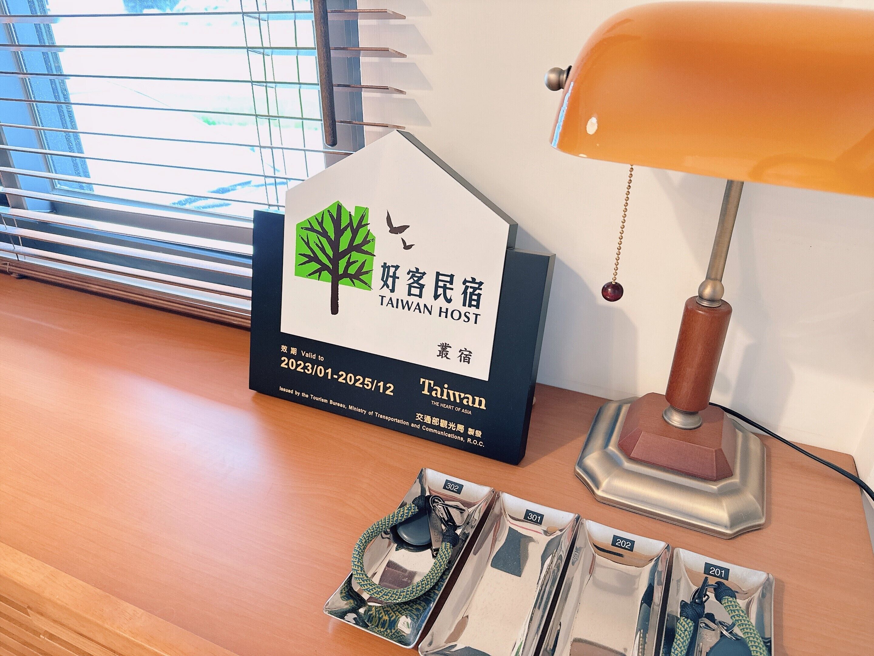 Een Taiwan Host bordje, een lamp en een dienblad met spullen op een houten tafel.