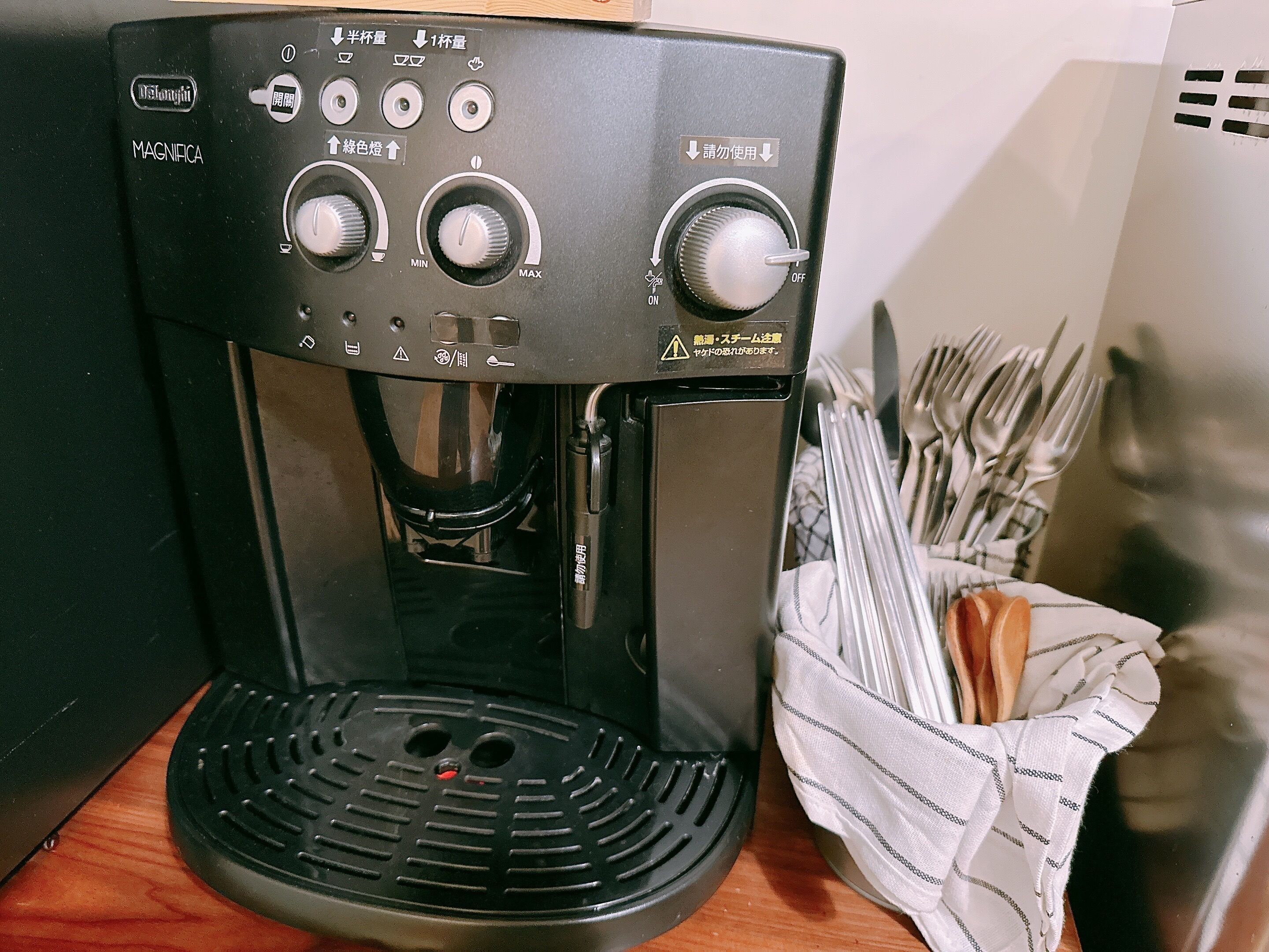 Een koffieapparaat met verschillende bedieningsknoppen en knoppen, een opvangbak en een servettenhouder met bestek.