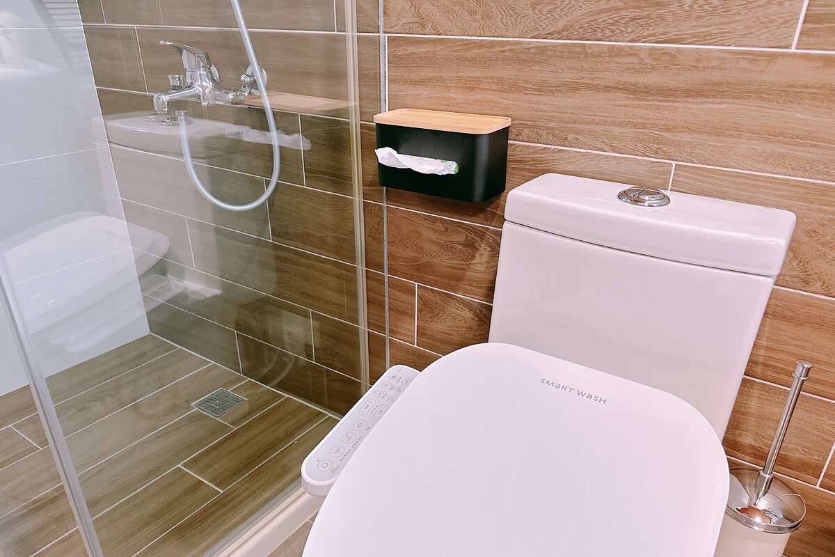 A modern bathroom with a glass shower enclosure, a white toilet, and a wooden shelf.