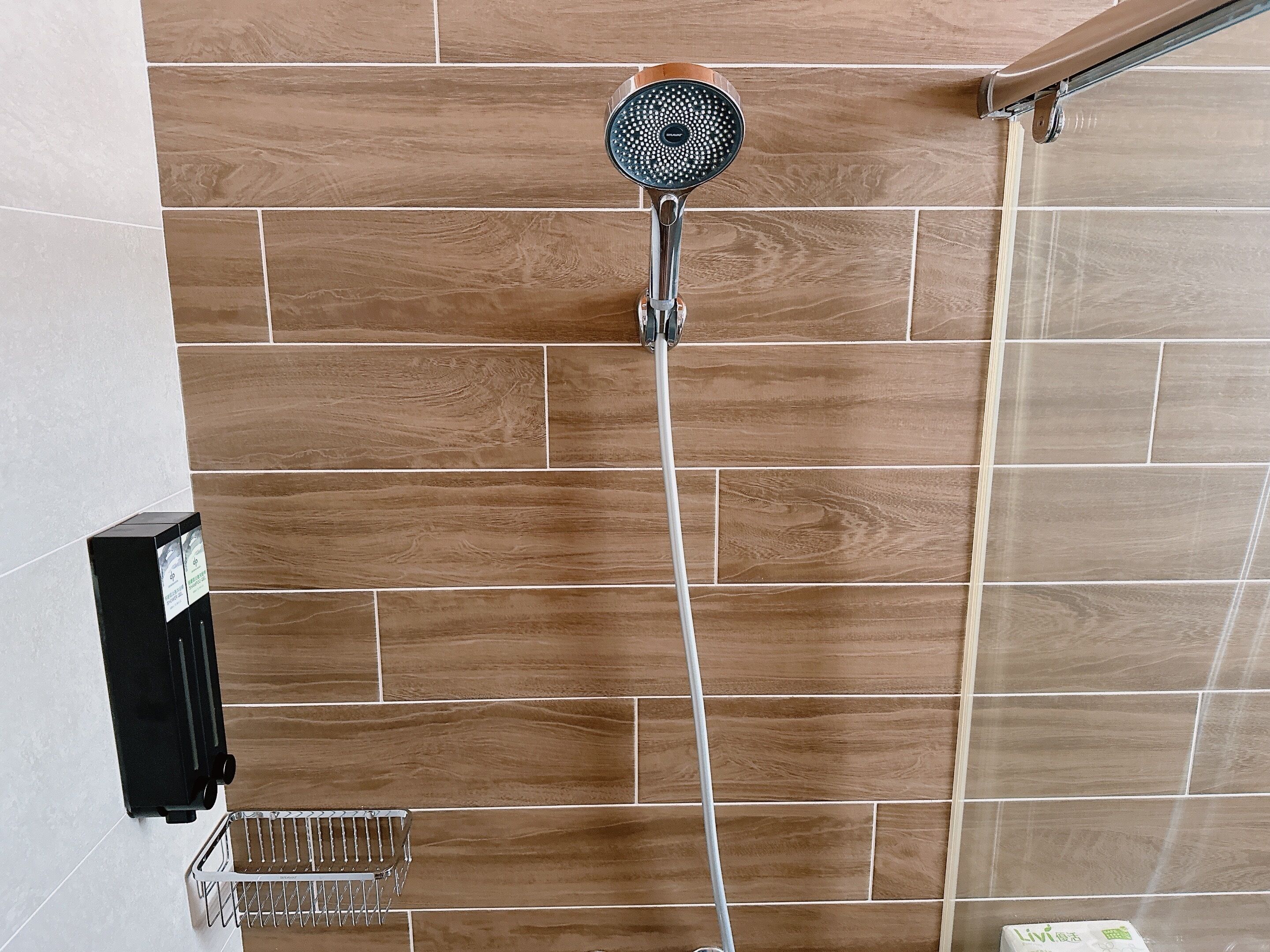 A shower with a handheld showerhead mounted on a wall with wooden tiles.