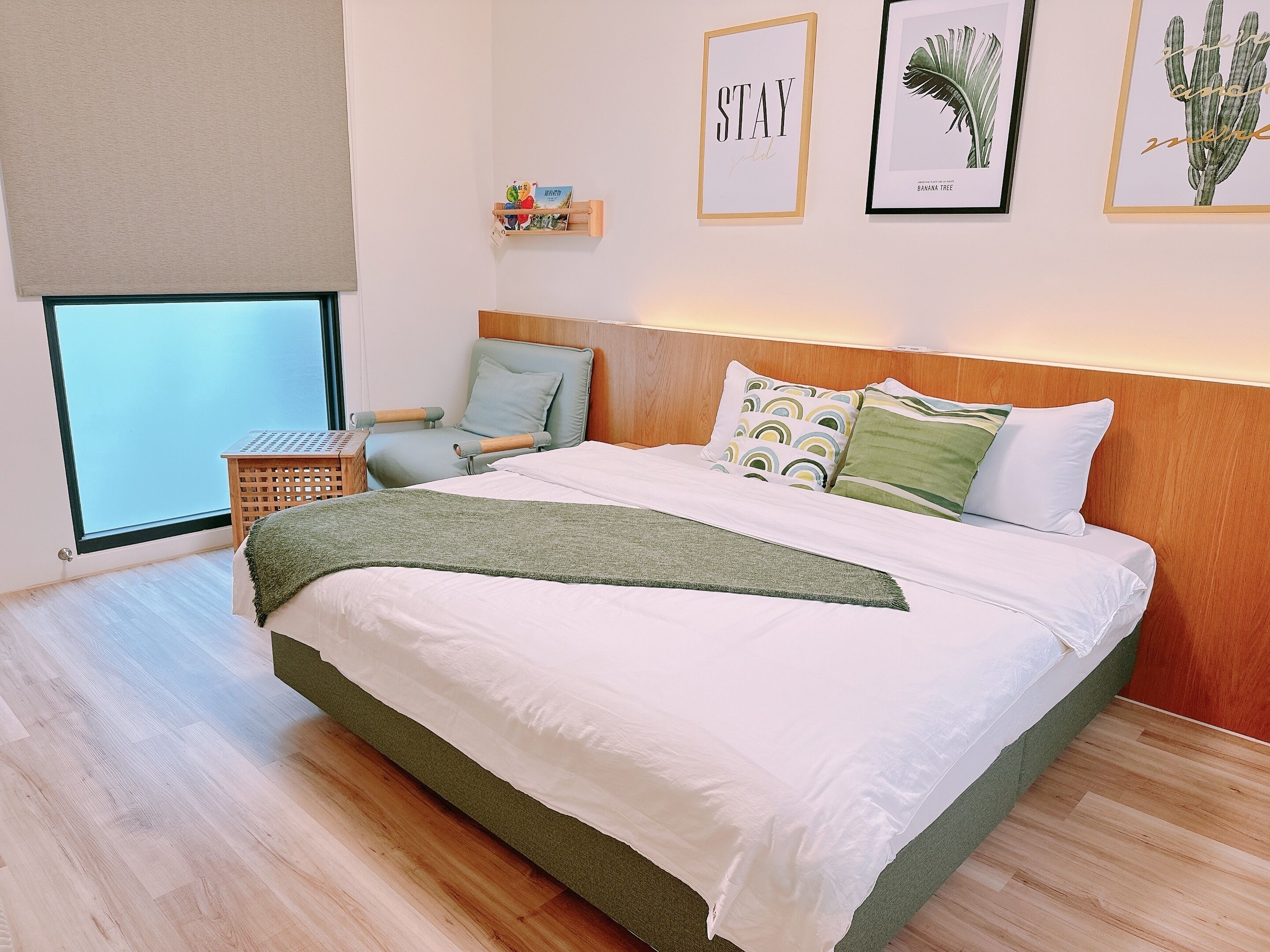 Een moderne slaapkamer met een groot bed, een stoel, een klein tafeltje en kunstwerken in lijsten aan de muur.