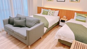 A modern hotel room with a grey sofa, two beds with green bedding, and a wooden headboard. - Gardenstay (Luodong)
