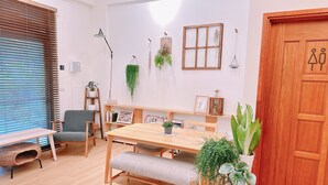 A cozy living room with a wooden dining table, a bench, a grey sofa, and a wicker chair. There are several potted plants, a wooden ladder, and a wall-mounted shelf with books and decorative items. - Gardenstay (Luodong)