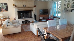 Een woonkamer met een open haard, een televisie en een eethoek met een tafel en stoelen.