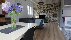 Un comedor con una mesa, sillas y un florero. Se observa una pared de piedra y un televisor al fondo.