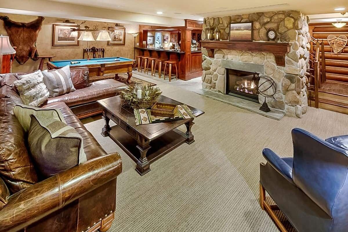 A cozy living room with a pool table, leather sofa, and a stone fireplace.