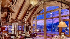 A spacious room with a large window, wooden ceiling beams, and a mounted moose head. - Eagles Nest Luxury Retreat, Views, Hot Tub, Walking distance to Resort (Sundance)