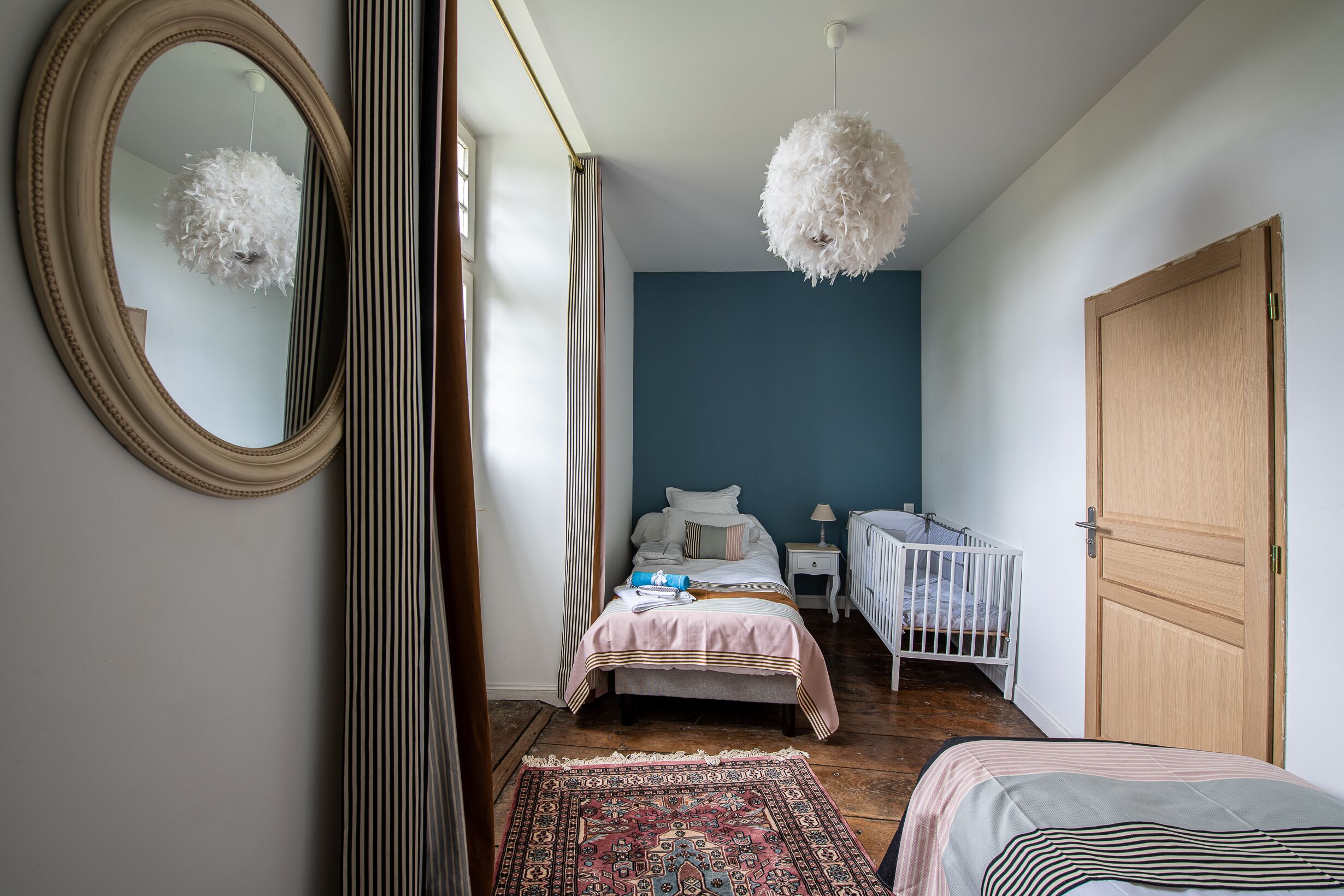 A bedroom with a bed, a crib, a mirror, and a hanging light fixture.